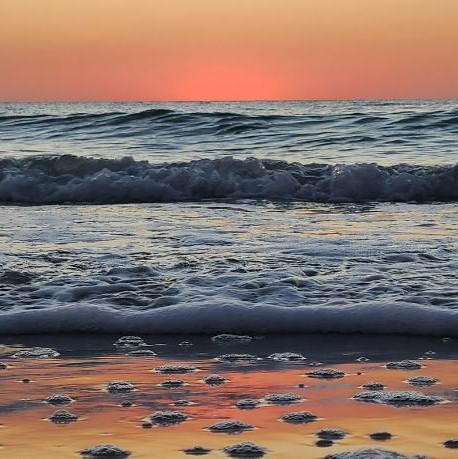 An orange and pink sunset with waves crashing on the beach